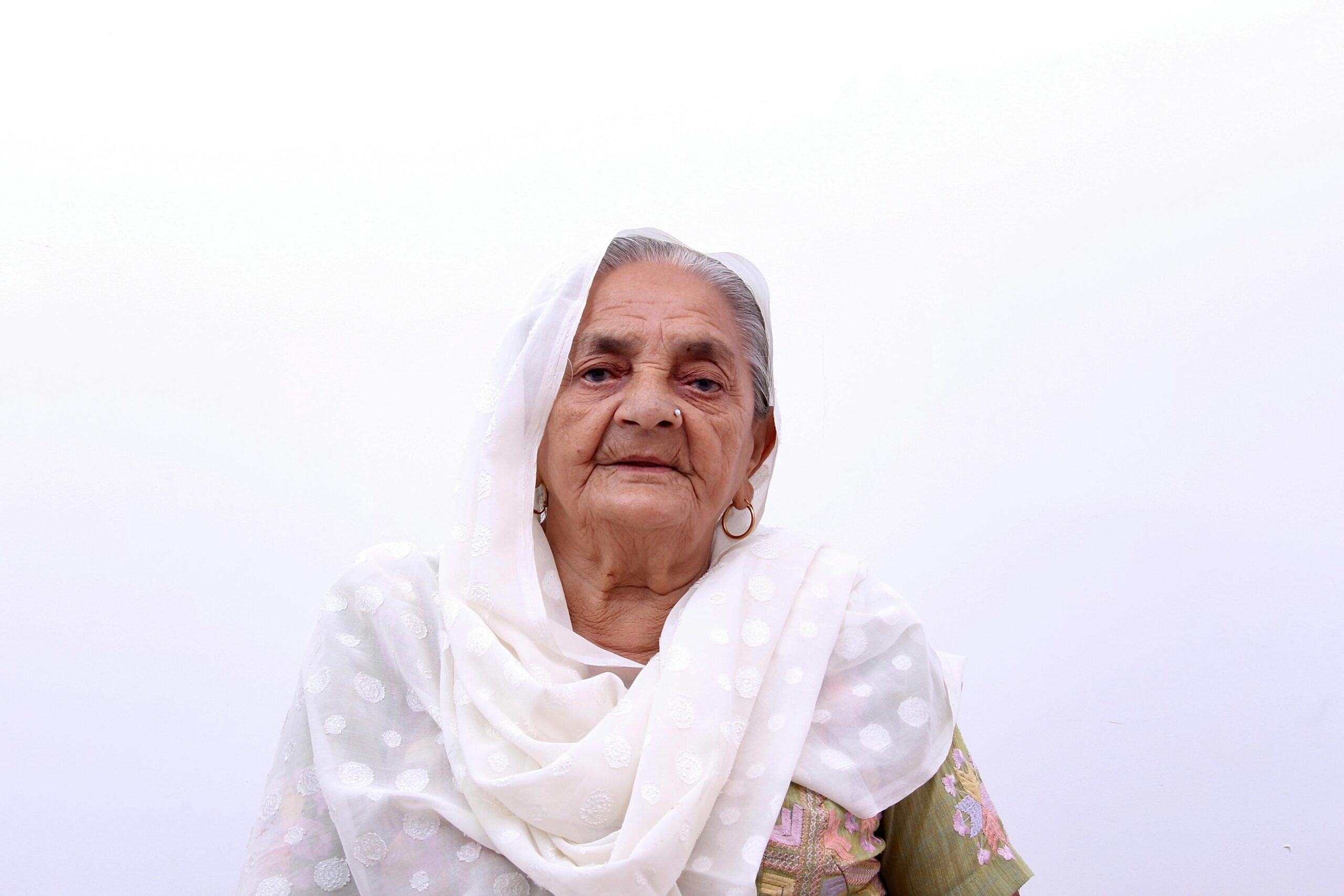 Portrait of an elderly woman in white traditional attire on white background.