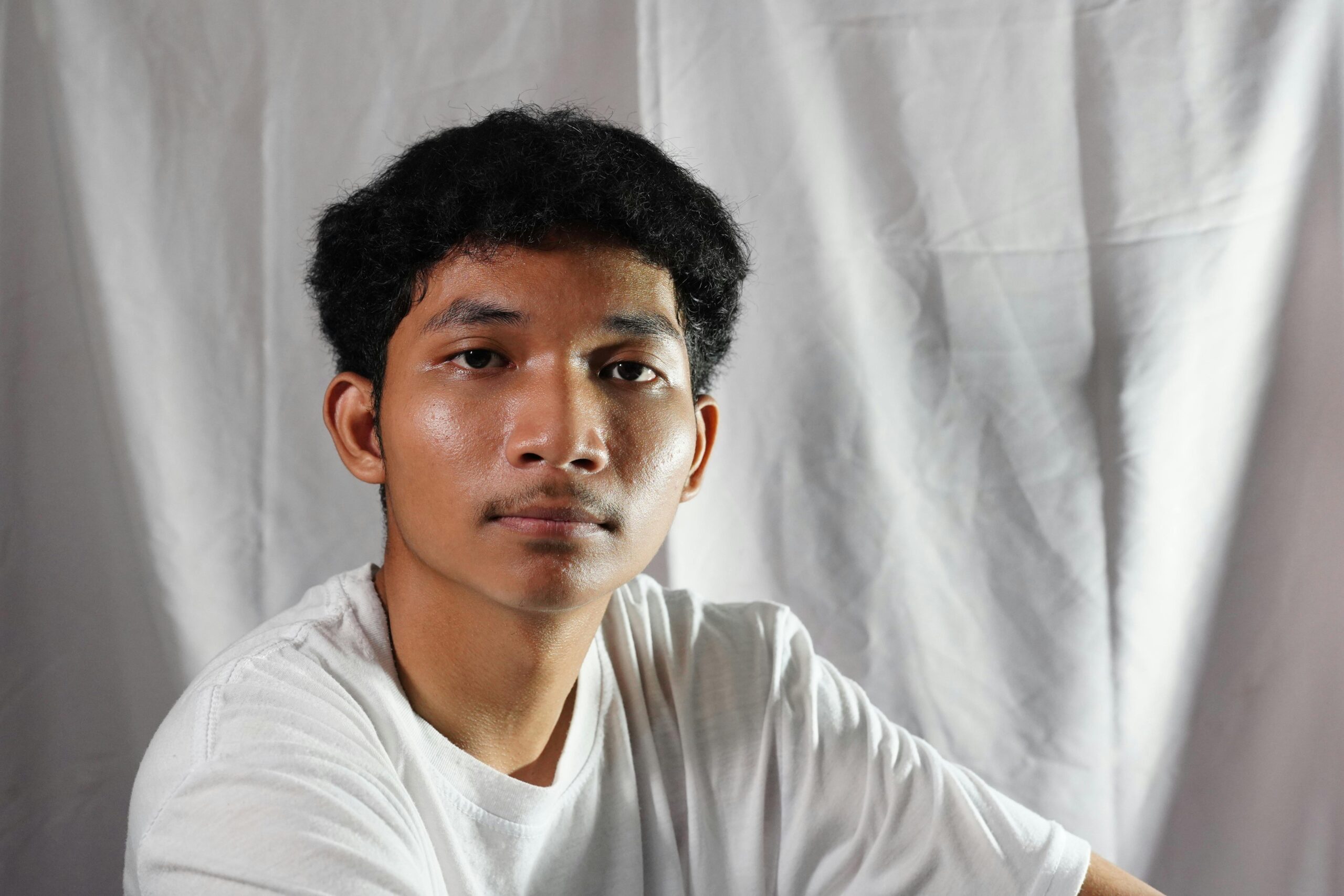 Thoughtful young man wearing white t-shirt against a plain backdrop.